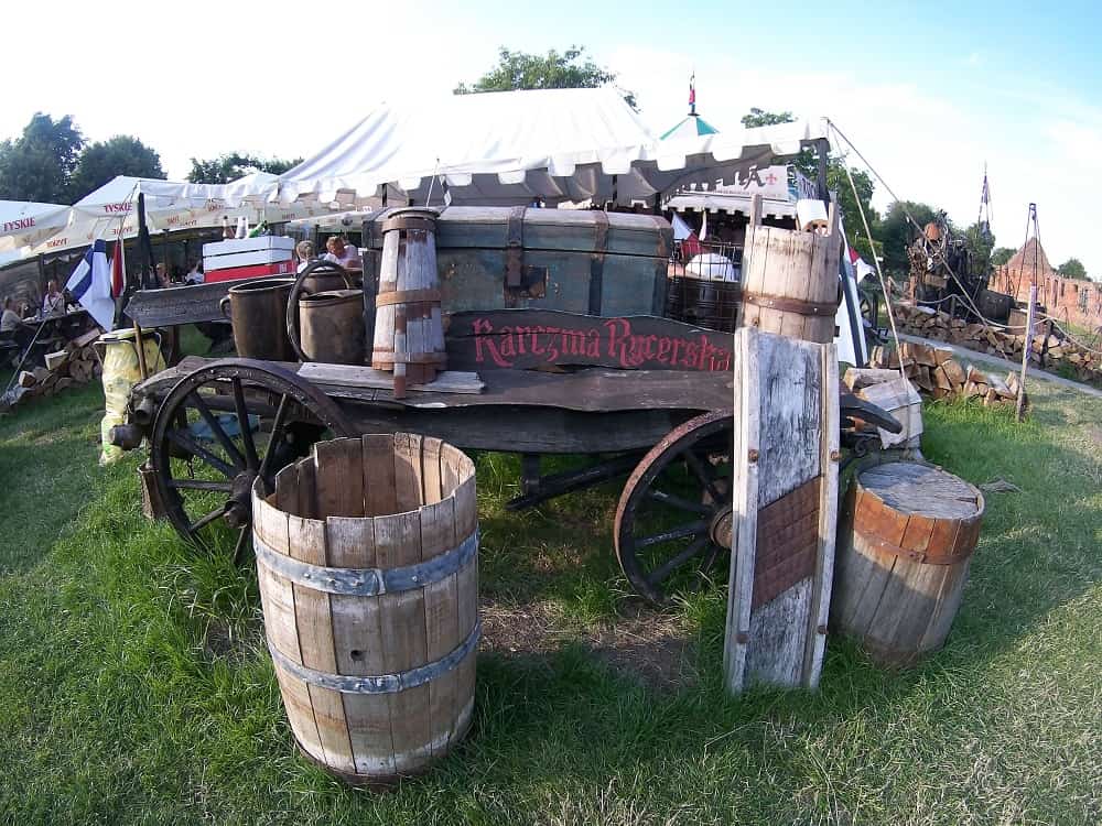 karczma rycerska pod zamkiem w Malborku. Stary wóz, beczki, w tyle namiot gdzie wydają jedzenie.