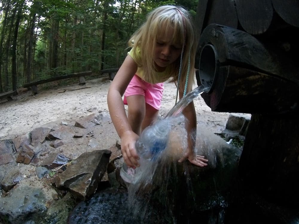 Dziewczynka napełnia wodą ze źródła św. Franciszka butelkę. Woda rozbryzguje się na boki.
