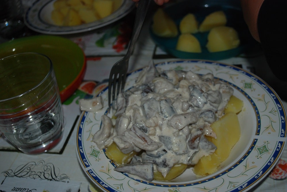 Kartofle z grzybami, na talerzu. obok pusta już szklanka w której dopiero co było wino.