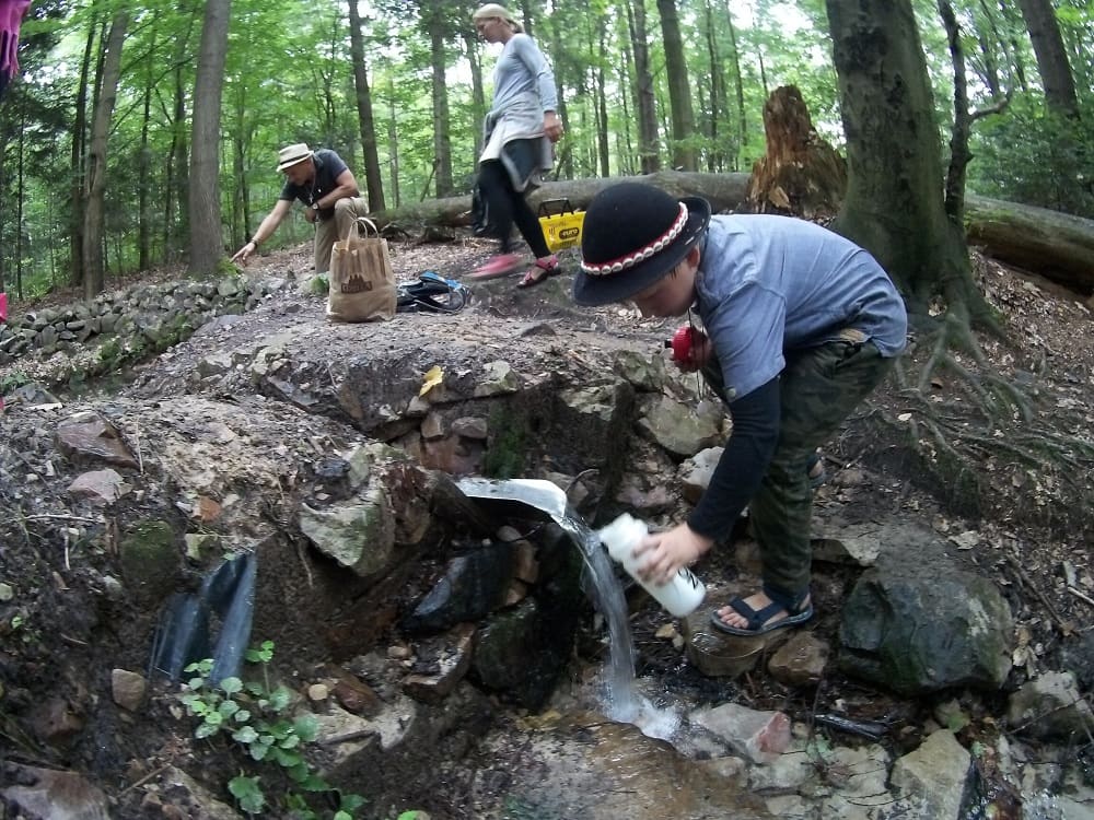 Chłopiec nabiera wody ze źródełka do bidonu