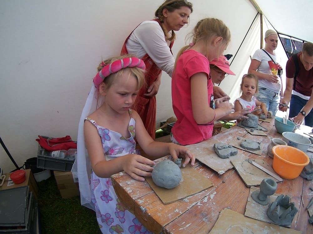 Dzieci pod okiem instruktorki lepią dzieła w glinie.Zuzia na pierwszym planie z wielką kulą gliny
