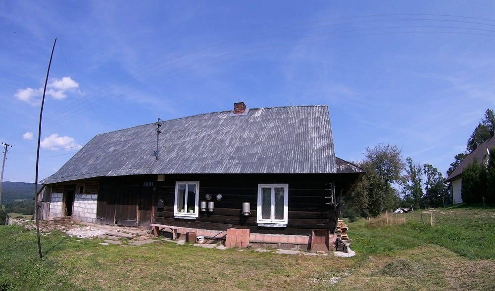Budynek drewniany, połączony z pomieszczeniami gospodarczymi. Na domu pomiędzy oknami wiszą kany na mleko.