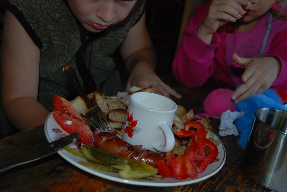 Chłopiec, dziewczynka. Przed nimi talerz ze smażoną kiełbasą, papryka,pokrojone ogórki kiszone, pomidory i grzanki.anie bacówkowe.