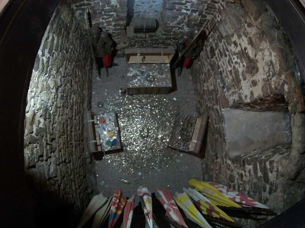 Kamienna piwnica, w niej skrzynie, monety, flagi.