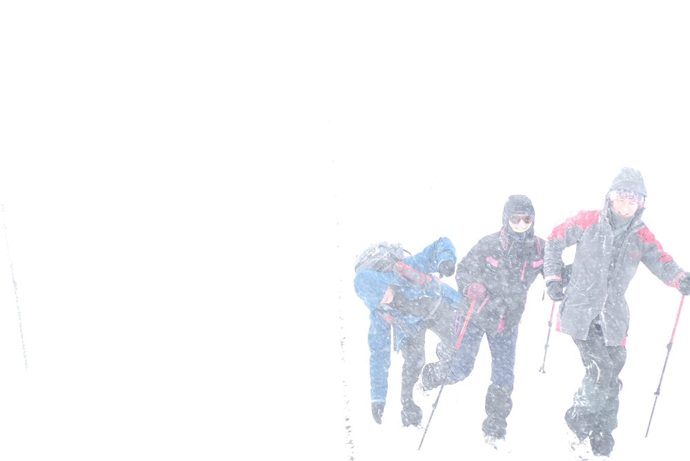 Trójka turystów zmagająca się z wiatrem. Trzy postacie ledwie wyłaniają się z bieli