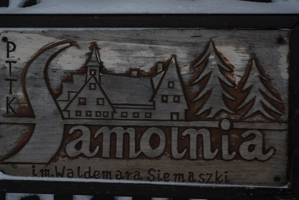 Drewniana tablica z ryciną budynku i napisem Samotnia im. Waldemara Siemiaszki