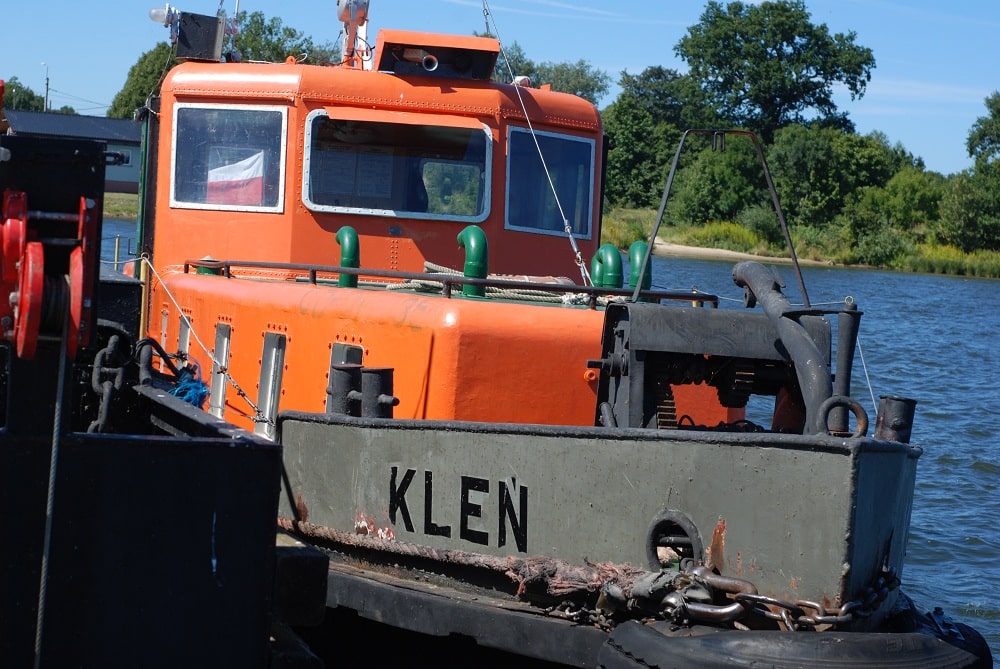 Holownik przy burcie promu.  Na pierwszym planie dziób łódki z nazwą KLEŃ